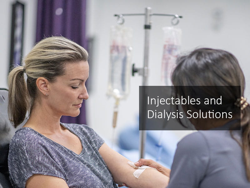 A nurse with dark hair holding an intravenous drip in place on a young woman in a hospital setting.