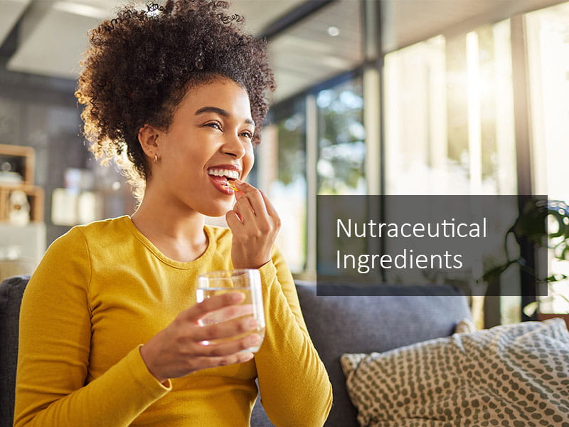 Young woman with brown hair, smiling as she holds a yellow nutraceutical capsule and glass of water