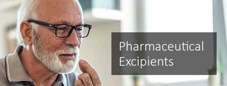 Older man with short white hair and beard, wearing glasses, taking a pharmaceutical tablet with a glass of water. 