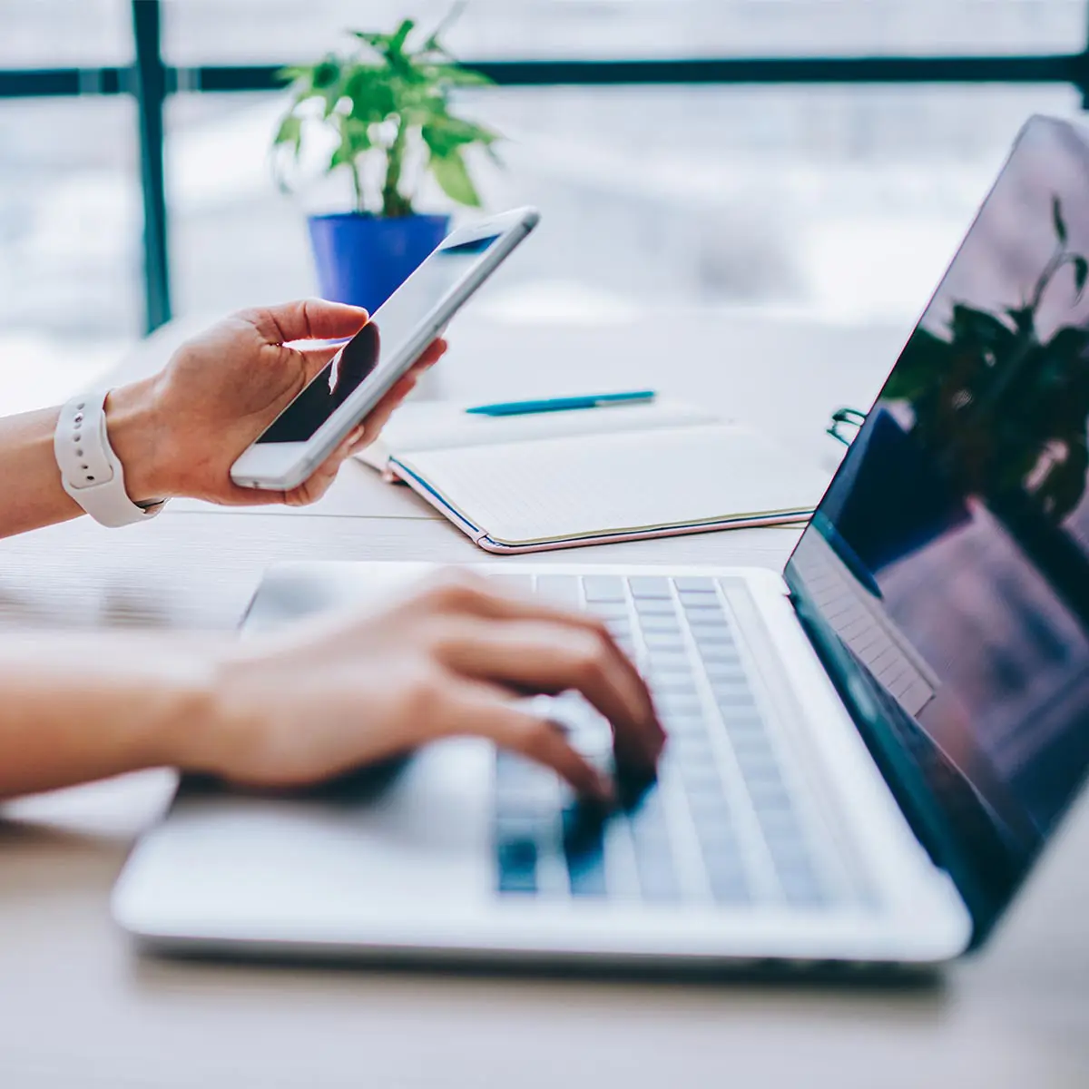 Person working at a desk with a laptop and a smartphone.