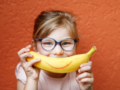 Smiling little girl holding a banana in front of her mouth