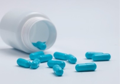 Blue capsules spilled from a white plastic bottle onto a light surface, arranged randomly.