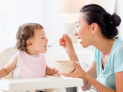 A woman is giving food with a spoon to her baby.