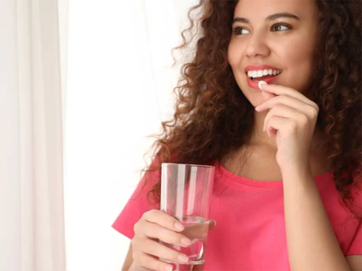 A young smiling woman swallows medicine with a glass of water