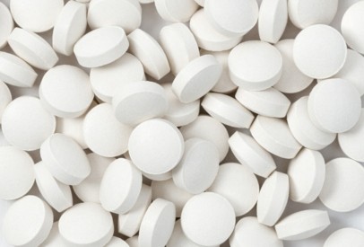 Close-up of numerous white, round tablets scattered across a surface, illustrating solid oral dosage forms and pharmaceutical formulation.