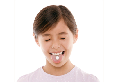 Close up of a child holding a white tablet on an outstretched tongue.