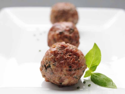 Three cooked plant proteins meatballs arranged in a row on a white plate.