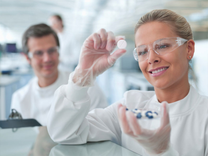 Scientist in lab coat and gloves examining a white tablet in a laboratory setting.
