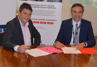 Two men sitting at a table signing documents in a formal business partnership setting.