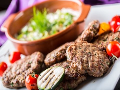 Grilled meat-likes patties served with zucchini, cherry tomatoes, and a fresh salad in the background.