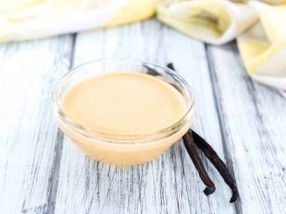 Bol en verre rempli de crème anglaise avec des gousses de vanille sur une surface en bois.