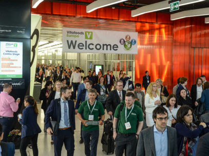 Crowd of people entering a convention center under a large “Welcome” banner at an event.