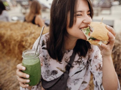 A woman eating a burger and drinking a smoothie