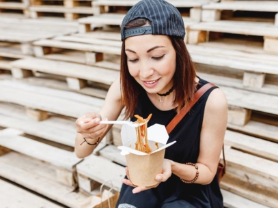 A woman sitting on stairs outside eating a pasta box