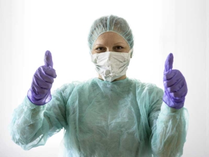 Personne en blouse de protection et gants violets levant les deux pouces.