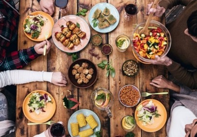 Healthy shared meal around a wooden table featuring fresh salads, fruit salad, plant-based skewers and nutritious foods supporting longevity and wellness.