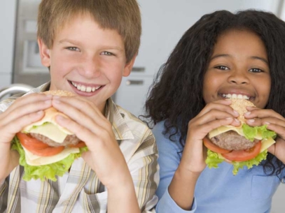 Deux enfants tenant et sur le point de manger de gros hamburgers avec salade, tomate et fromage