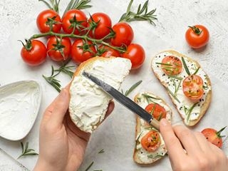 Hands spreading cheese with a knife on a slice of bread