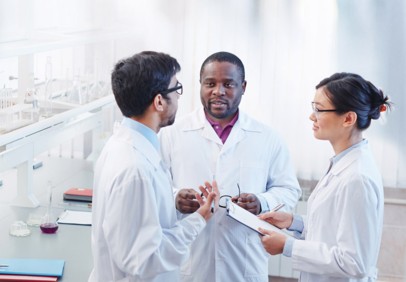 Trois scientifiques en blouses blanches discutent ensemble dans un laboratoire avec du matériel scientifique.