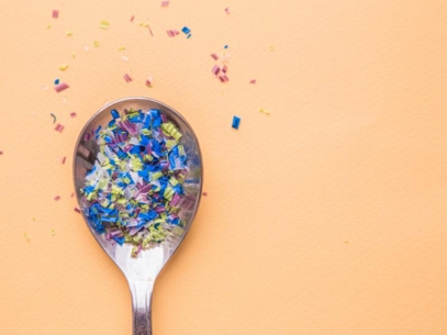 A spoon filled with small pieces of plastic on an orange background