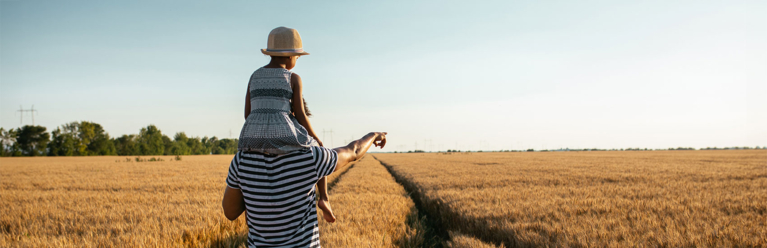 Un homme porte sa petite fille sur ses épaules et lui montre l'horizon, devant un champ de blé.