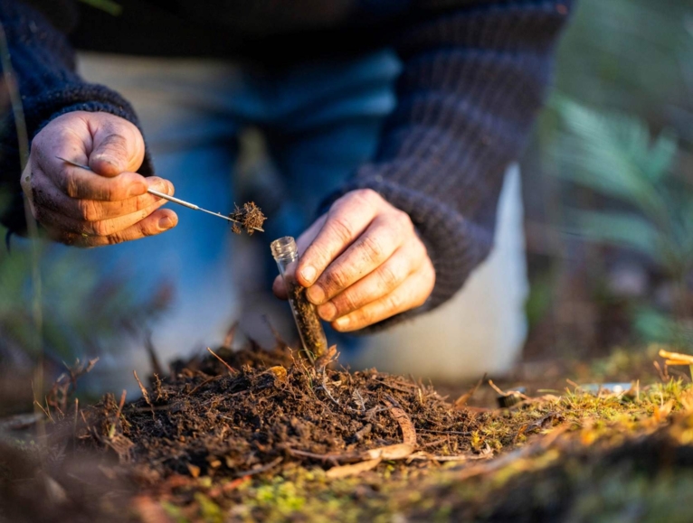 Man crouching in a field taking a soil sample