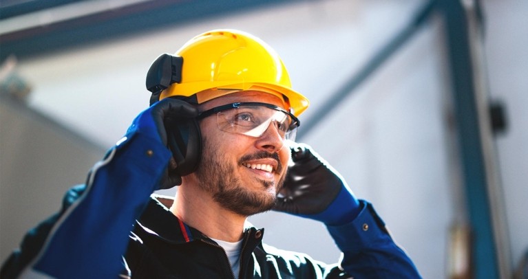 Un ouvrier portant un équipement de protection, avec un casque jaune, des gants et une protection auditive, dans un environnement industriel.