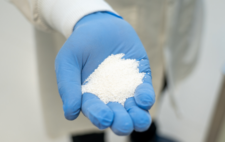 Une main gantée tenant une petite quantité de poudre blanche de maltodextrine dans un environnement industriel.