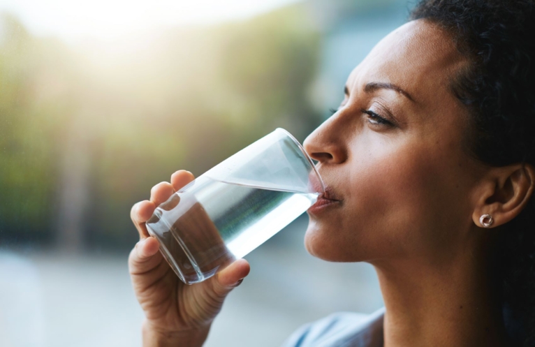 Woman with dark hair drinking water from a glass cup in daylight