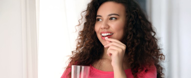 Young woman in pink top about to take a tablet with a glass of water.