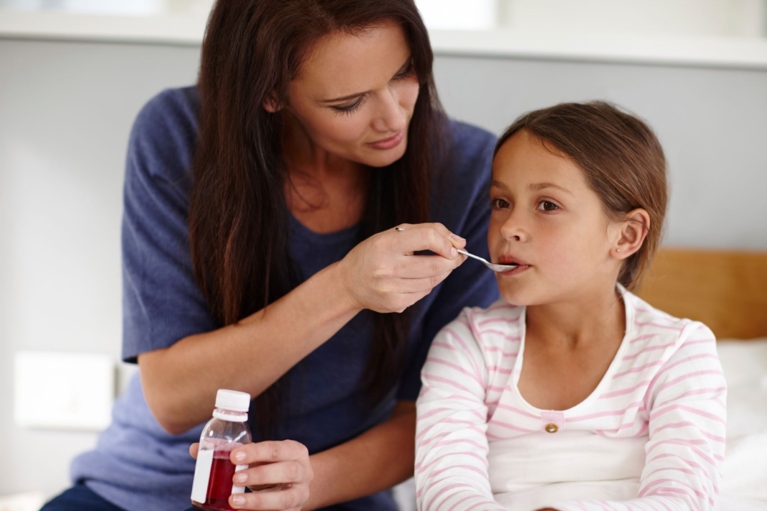 Close up of a woman feeding a spoonful of medicine to a young girl
