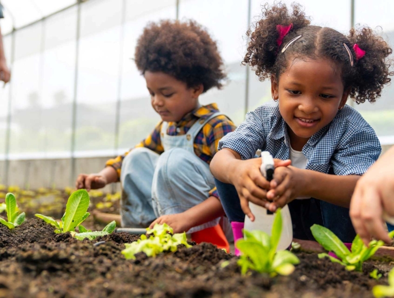 Two ittle girls in a greenhouse watering plants
