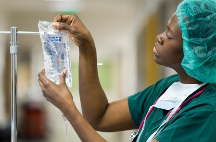 A nurse placing a dialysis bag on a metal stand in a hospital setting